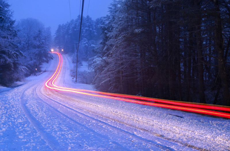 The tail lights of a car traveling down a road during a spring snowstorm leave a light trail Friday in this 30-second time exposure in Freeport.