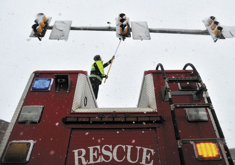 Waterville Fire Department Lt. Scott Holst clears the traffic light sensors free from snow Friday at the Post Office Square intersection in Waterville on Friday. Heavy snow wreaked havoc during the morning Friday, covering the sensors and setting lights on an unyielding red.