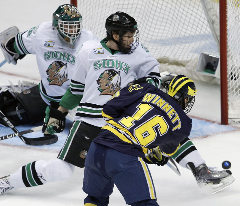 GETTING THROUGH: Michigan left wing Ben Winnett, right, shoots the puck under the skate of North Dakota defenseman Derek Forbort, center, to score on North Dakota goalie Aaron Dell during the first period of a Frozen Four semifinal Thursday night in St. Paul, Minn. That goal proved to be the game-winner as Michigan upset North Dakota 2-0 to reach Saturday night's championship game against Minnesota-Duluth.