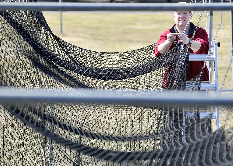 GETTING READY: Greg Stewart hangs up a batting cage net Saturday morning at Morton Field in Augusta. Stewart and other volunteers were working around the complex shoveling snow from in front buildings and getting the fields ready. Most of the complex was snow-free but some piles lingered in shady spots.