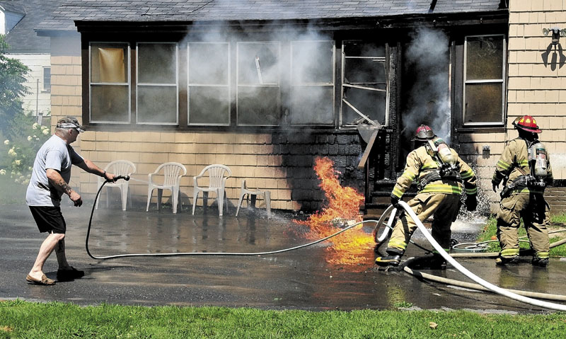 NEIGHBORLY HELP: Neighbor Rick Burgess Sr. uses his garden hose along with Waterville firefighters to douse flames at a residence on May Street in Waterville on Saturday. Deborah Kilsby and Randy LaPointe also helped rescue a dog from the home.