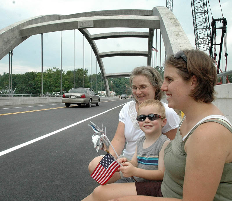 Zachary Niederfringer, 4, waves a flag and pinwheel at cars passing for the first time over the new bridge that spans the Kennebec River on Thursday in Norridgewock. He sat with his mother, Rebecca, and grandmother, Janice Malek, who lives next to the bridge. Zachary said he can’t wait to ride his bike across to the other side.