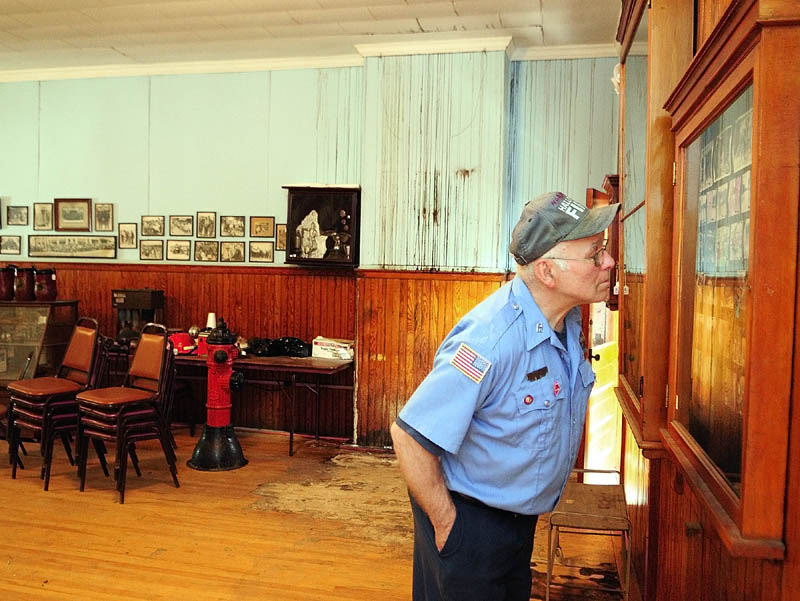 Hallowell Fire Department engineer Norman Cormier looks at photos in a display case in the upstairs meeting room on Thursday during a tour of the Hallowell fire station. The marks on the wall and floor behind him are creosote and mold stains caused by roof leaks.