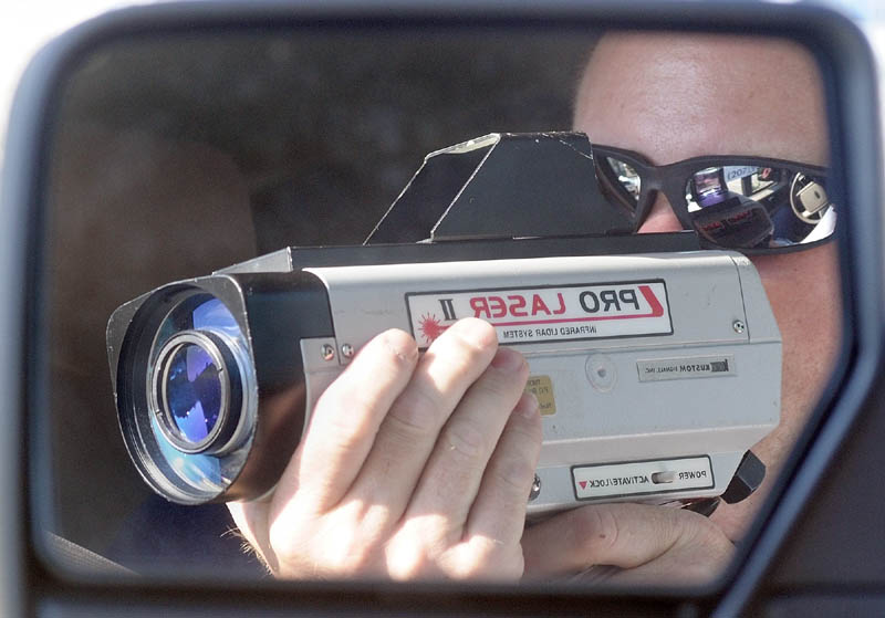 Sgt. Christopher Shaw is reflected in the mirror of an unmarked sport utility vehicle while he points a laser gun to clock the speed of oncoming during a speeding enforcement detail Friday morning on Western Avenue in Augusta. When he spotted a speeder he dispatched one of four officers after the car.