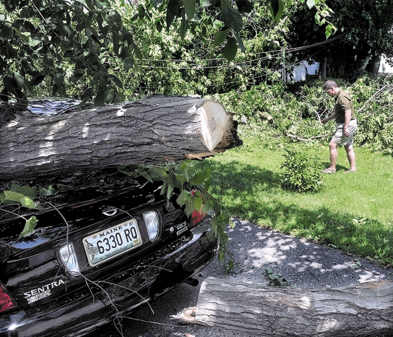 THE STORM’S AFTERMATH: Apartment owner Derik Saucier on Thursday walks past fallen power lines and trees that cover and damaged his building and a neighbor’s vehicle during a violent storm Wednesday night on School Street in Waterville.
