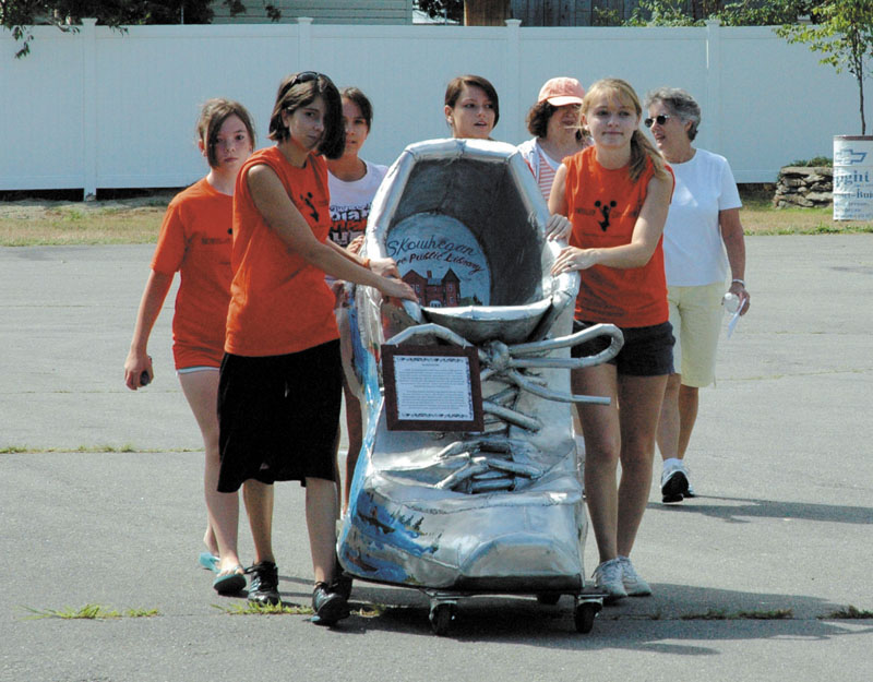 ONE GIANT STEP: Skowhegan Library Director Dale Jandreau, right, directs cheerleaders from Skowhegan Area High School onto the state fairgrounds Tuesday with the library’s Giant Shoe sculpture, which recognizes the area’s shoe-making heritage and promotes youth fitness. The shoe will be on display in Constitution Hall for the duration of the fair, which opens Thursday.