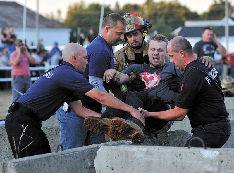 NO PAIN, NO GAIN: Matt Davis is helped over the Jersey Barriers of the demolition derby arena by Skowhegan firefighters after being injured in the second heat of the Skowhegan State Fair annual demolition derby on Aug. 12.