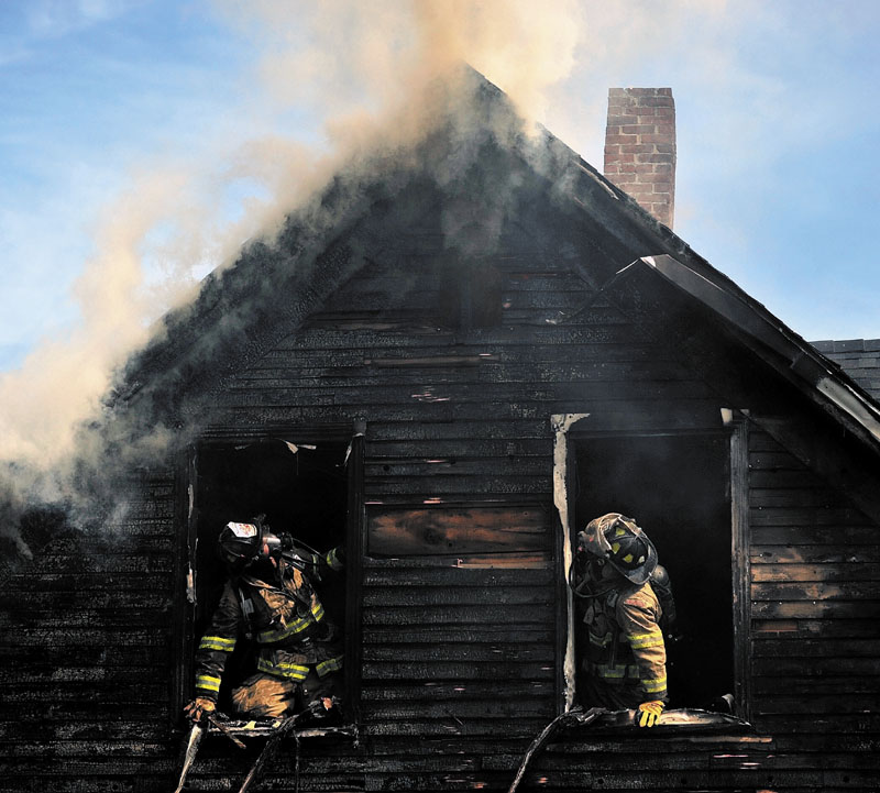 DESTROYED: Firefighters are seen in the charred windows of a house on Oak Street in Waterville Tuesday morning. A family of four was left homeless by the blaze.