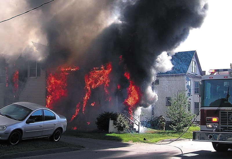 ON FIRE: A house on Oak Street in Waterville is consumed by flames Tuesday morning as firefighters arrive on the scene.