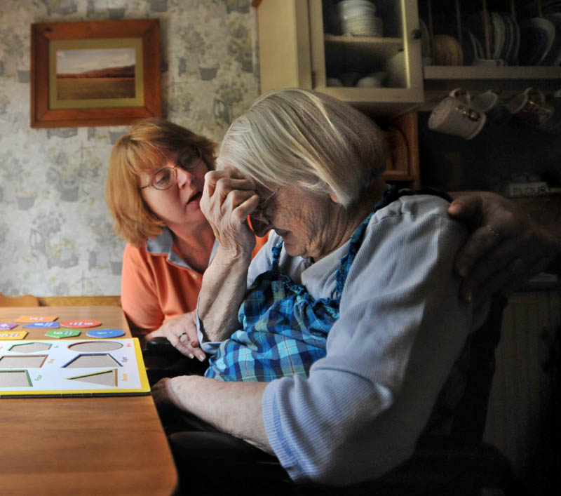 Cheryl Barkow, back, comforts her mother, Alice Osborne, 93, as she tries to complete a puzzle at the kitchen table at Barkow's New Sharon residence recently. Barkow and her husband Larry care for Cheryl's mother, who has dementia.
