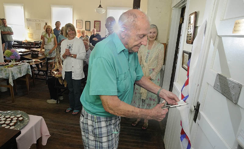 Tom Adell cuts the toilet paper ribbon to ceremonially open the Barbara H. Fogg Necessary Room on Friday evening at the Readfield Historical Society.