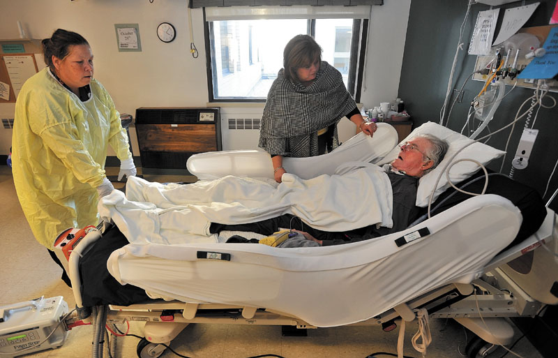 CARE AND COMFORT: Jan Homer places a hand on her father, David Brophy as CNA Jessie Rowe checks in during his treatment at Thayer Hospital in Waterville Friday afternoon. Brophy was critically injured in an auto accident on outer Clinton Avenue in Winslow when a dump truck collided with him as he pulled out of his driveway.