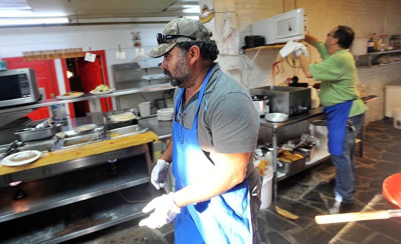 PITCHING IN: Myao Perez, center, hustles in the kitchen at Cancun Mexican Restaurant in Waterville as Hector Fuentes, back right, prepares food for the dinner rush Tuesday. Perez is one of many friends of Fuentes who has volunteered his time to help his friend keep his business open after several workers were arrested on charges of illegal immigration.