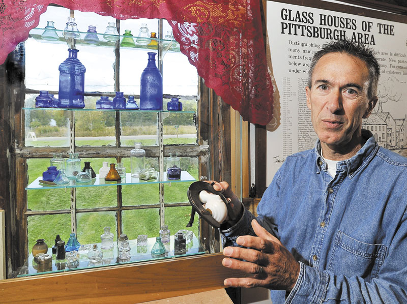 COLORFUL DISPLAY: Walter Bannon shows one of the more interesting glass objects — a milk glass snail shaped ink well that opens and closes to keep the ink fresh — Wednesday at his Maine Antique Bottle and Glass Museum in Bridgton.The bottle is attached to a real horseshoe with an attached horse leg to keep it stable during use, according to Bannon. In the window is a collection of glass ink bottles of various shapes and colors.