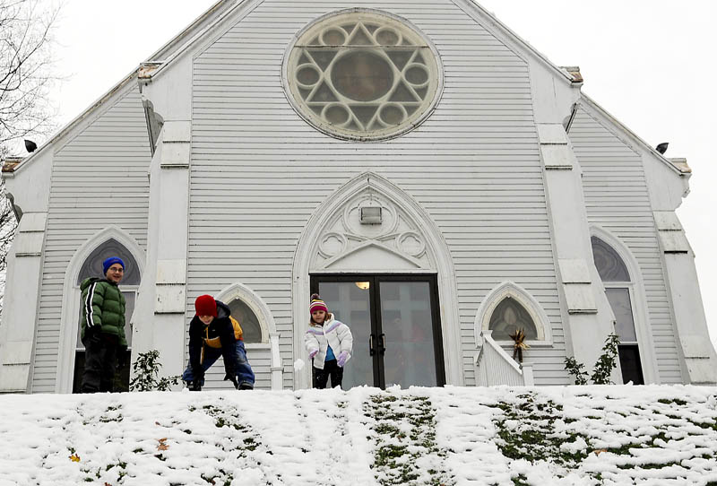 Robby, 12, left, Kenny, 10, and Abby Allen, 5, roll snowballs Sunday down the hill in front of Sacred Heart Church in Hallowell. The siblings were waiting for their grandparents, Mary and Raymond Moinester, to emerge after Mass to a landscape filled with snow.