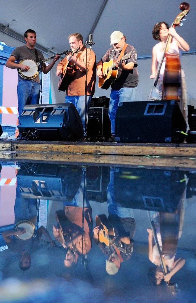 The Phat Grass band is reflected in a puddle in the middle of Water Street as they perform during Swine & Stein festivities Saturday on Water Street in downtown Gardiner.