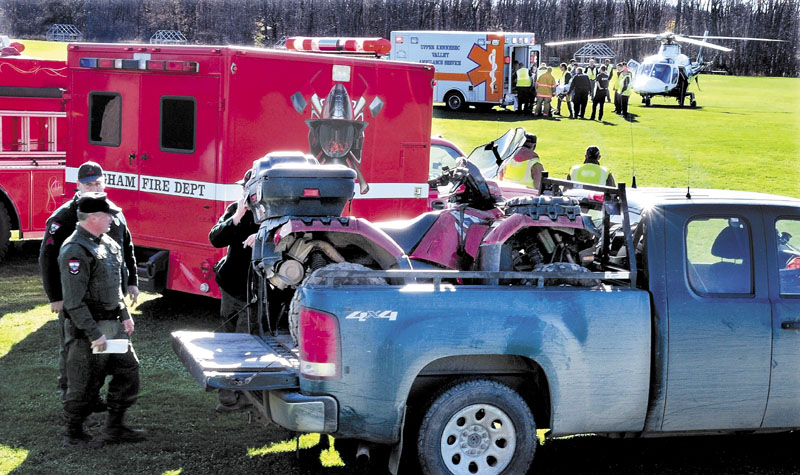INJURY: Game Warden Rick Clowry, front, and other wardens look at an all-terrain vehicle that lost a rear wheel, sending operator Glen Dow of Madison into a ditch while he was riding in Caratunk on Sunday. Dow is being loaded into a LifeFlight of Maine helicopter at an airport in Bingham.