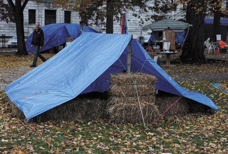 OCCUPY: A pedestrian passes an Occupy Maine protester's tent insulated with hay bales on Tuesday in Lincoln Park in Portland. Protesters are preparing for the colder weather and vowing to stick it out through the winter.