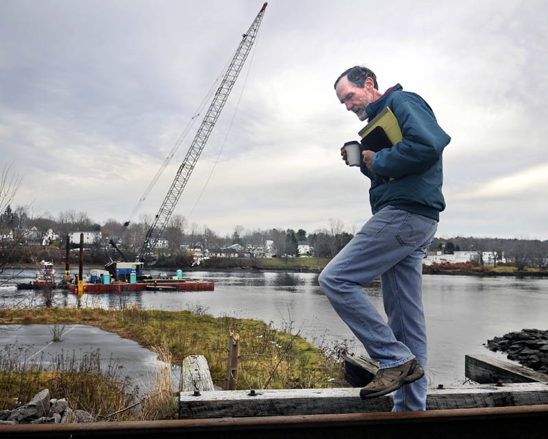 PARALLEL PATHS: Logan Johnson strolls Monday across the trestle over Cobbossee Stream at the confluence of the Kennebec River in Gardiner as a Cianbro barge pulls a crane to the firm's dock in Randolph. Johnson, a city councilor, was walking the tracks next to where he once netted sturgeon with his late friend, Brian Rines, to recover roe for caviar. The crane, according to workers on the CMP transmission line project, was being fitted with a shorter boom to resume tower construction on Brown's Island on the river between Chelsea and Farmingdale.