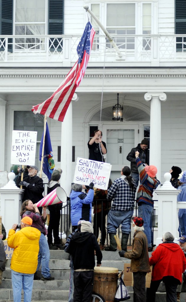 Protesters hoist a flag embroidered with "99%," along with the American flag, Sunday at the Blaine House during a protest by Occupy Augusta. Police say nine people were charged with criminal trespass and failure to disperse during the protest at the governor's mansion in Augusta.