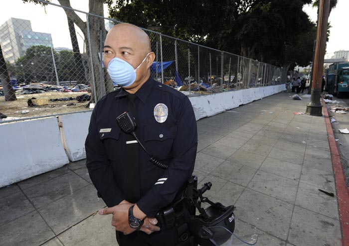 A Los Angeles police officer stands guard as city crews clean up and erect a fence around City Hall after the LAPD broke up the large encampment of protesters who had been camping there for the past two months.