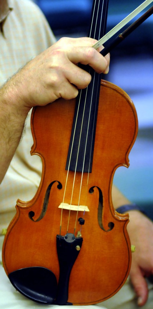 Nate Saunders holds his homemade violin, named after his wife, Cordelia, during a rehearsal Wednesday with the Augusta Symphony Orchestra in Manchester.