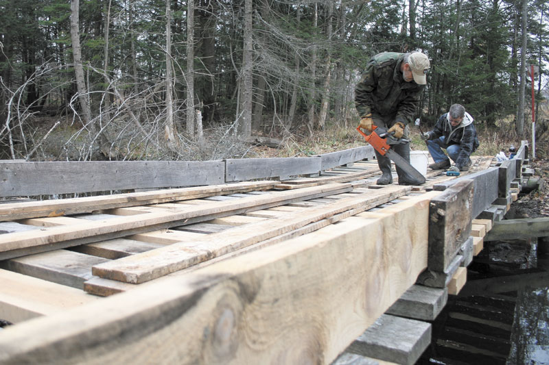 FIXING THINGS UP: Robert Bickford, left, cuts boards while Eric Roberts drives nails on a snowmobile bridge Sunday in Waterville. Due to a shortage of volunteers, the two men perform all of the yearly maintenance for Central Maine Snowmobile Club’s trail system. Many of Maine’s 287 snowmobile clubs have difficulty finding volunteers to maintain the state’s 14,000-mile trail system.