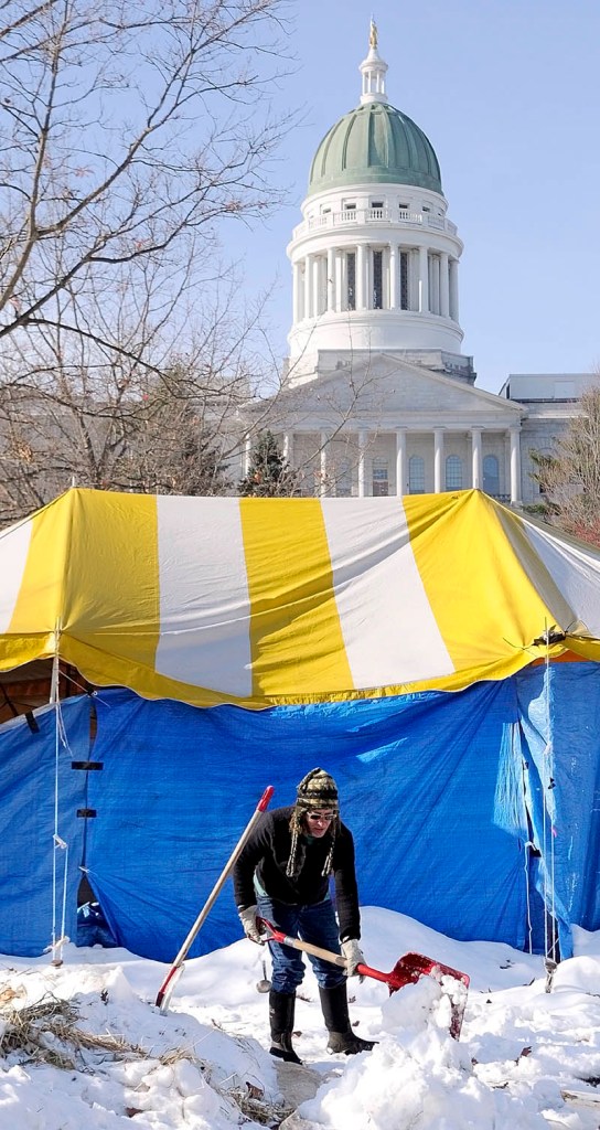 PREOCCUPIED: Jenny Gray, of Wiscasset, shovels snow onto a tarp in the Occupy Augusta encampment Friday morning in Augusta’s Capitol Park. She and several other people were clearing snow piles from the area.