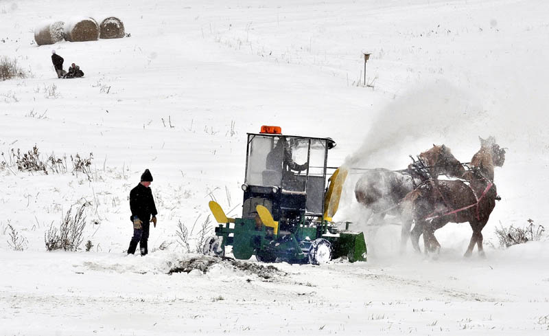 SNOW WORK: Amish farmer Andrew Stoll guides his horses as they pull a diesel snowblower while clearing a road in Unity on Saturday. His son Raymond watches the progress as other kids are pulled on a sled.
