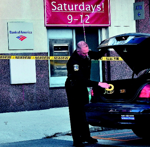 CRIME SCENE: Waterville police officer Tim Hinton finishes taping off the front and rear of the Bank of America on Main Street in Waterville after a male entered the bank on Monday with a suspicious bag and left with an undetermined amount of money. The man was arrested nearby on suspicion of robbery.