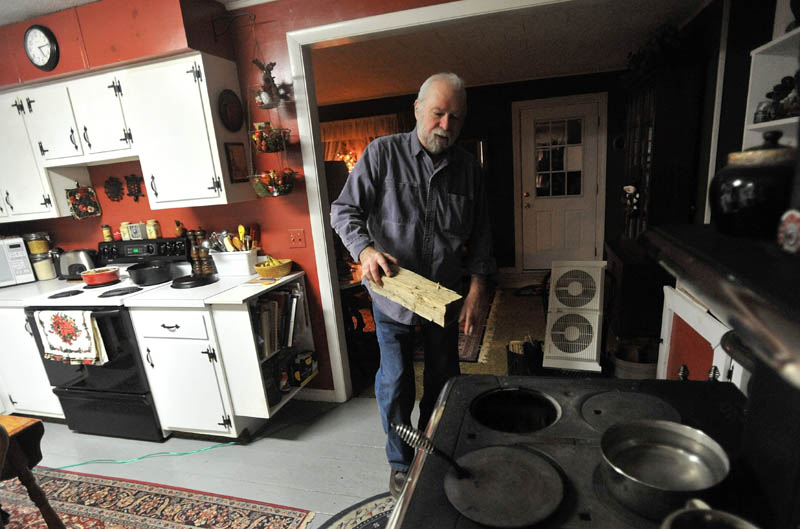 KEEPING WARM: Jay Adams places another log in the stove at home in Phillips on Thursday.