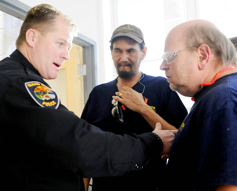 Idaho Falls, Idaho, Police Officer Malin Reynolds, left, shows Tex Tech Industries employee Bill Czerepanyn, right, and Frank Patten the spot where a bullet struck his chest vest during an open house at the Monmouth company Monday. Reynolds, who was shot in June 2011, credits the components in his body armor created by Tex Tech with saving his life.