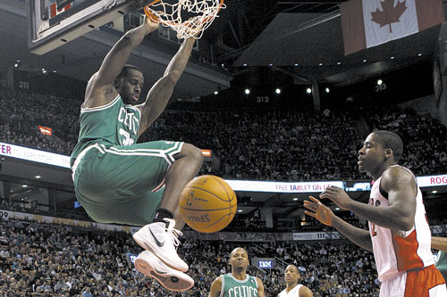 SLAM IT DOWN: Boston’s Brandon Bass, left, hangs from the basket after scoring as Toronto’s Amir Johnson looks on during the first half of a preseason game Sunday in Toronto.
