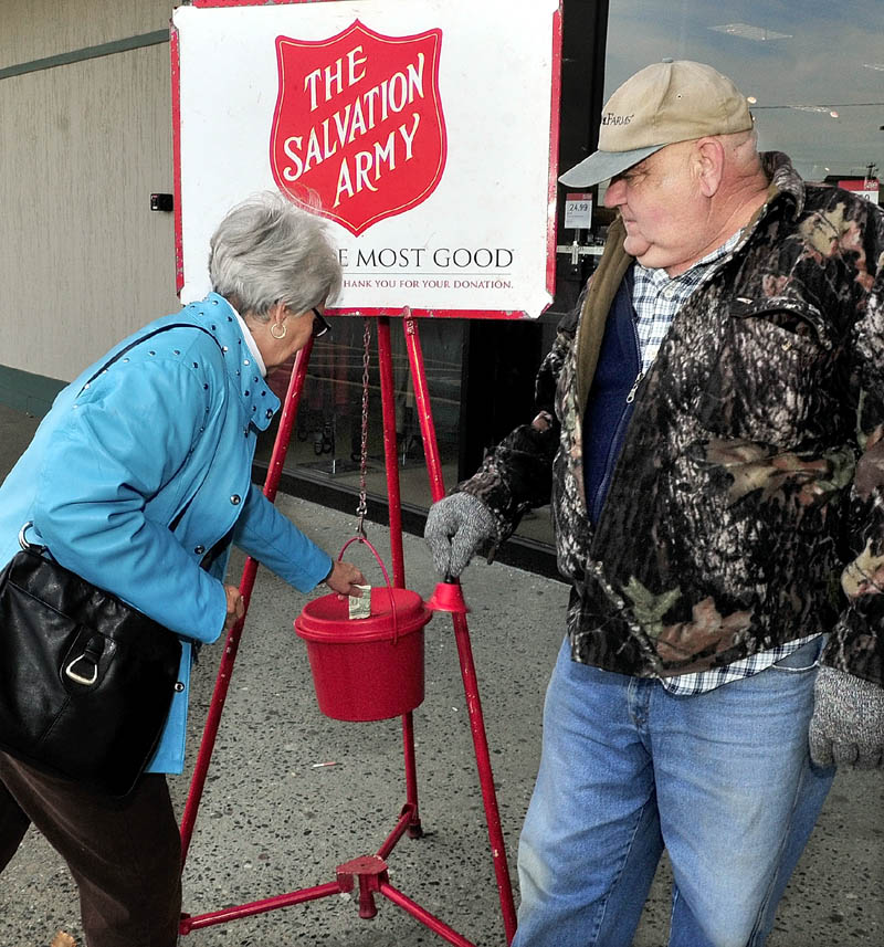 SALVATION: Salvation Army bellringer Donald Peace watches as Joyce St Pierre donates in front of the J.C. Penney store in Waterville on Tuesday. Maj. Karin Dickson said the Waterville organization has only reached a portion of its goal this year to fund services and is anxious for more volunteer bellringers for the annual holiday Kettle campaign.