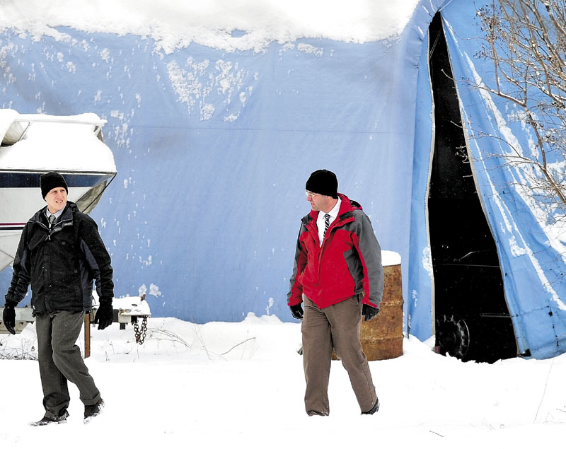 SEARCH: Two detectives walk past an outbuilding and a boat after searching the area outside a home on Whitehouse Road in Vassalboro on Tuesday after a 22-year-old man was shot.