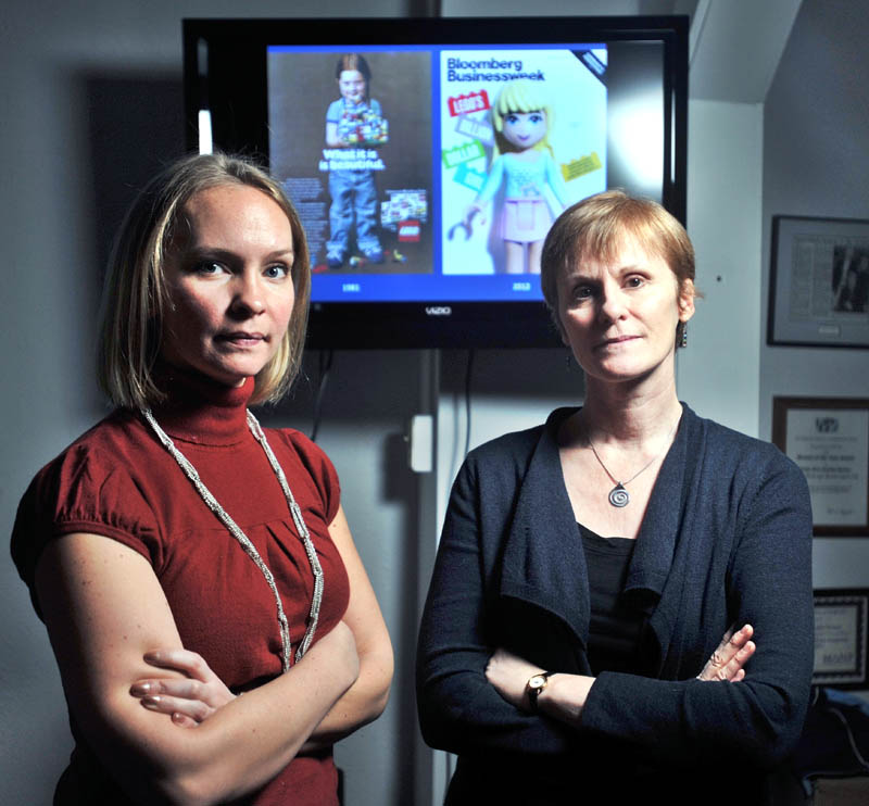 SAYING NO TO LEGO: Megan Williams, left, president of Hardy Girls Healthy Women, and Lyn Brown, a professor at Colby College, stand in front of two Lego advertisements at the Hardy Girls Healthy Women office in Waterville on Friday. The women are behind a protest of a new Lego line.