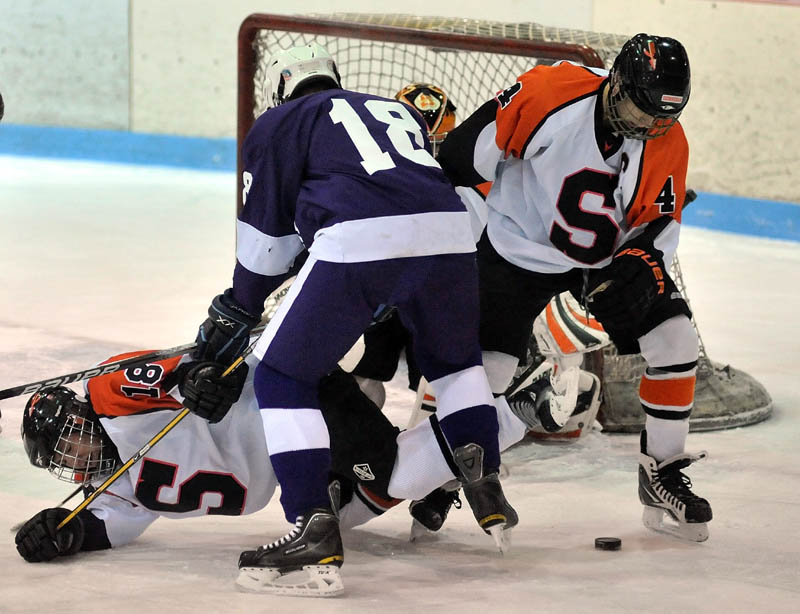 CREATING TRAFFIC: Hampden Academy’s Matthew Closson, center, knocks Skowhegan Area High School’s Anne Marie Provencal, left, to the ice as teammate Cam Despres tries to clear the puck from the front of Skowhegan’s net during the first period Wednesday night at Sukee Arena in Winslow. Skowhegan lost 5-3.