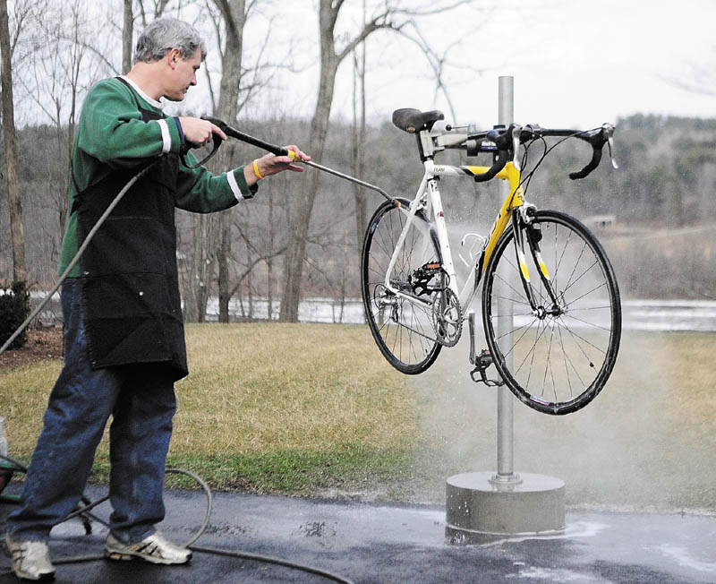 BIKE BATH: With grass and the open waters of the Kennebec River in the background, John Waller washes a bike he was servicing Thursday afternoon at Mathieu’s Cycle and Fitness in Farmingdale.