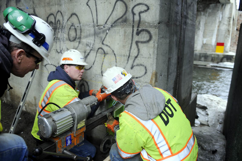 BORE THE BRIDGE: Maine Department of Transportation workers, from left, George James, Eric Moody and Keith Bates, level a drill Wednesday to bore a hole through a bridge column suspending the span across Cobbossee Stream in Gardiner. State crews have commenced work at repairing the concrete columns beneath Bridge Street and expect to be under the bridge through spring, James said. The drill bored a hole for a steel tension rod to be inserted into the column, James said.