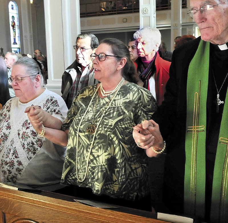 TOGETHER: Katheryn Moses, left, Linda Hook and Father Miles Brookes hold hands as they, and the congregation, recite the Lord’s Prayer during the final mass at St. Francis de Sales Church in Waterville on Sunday.