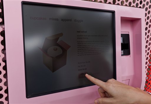 The machine features a touchscreen and a robotic arm that pulls cupcakes from a wall of single-serving boxes inside the store.