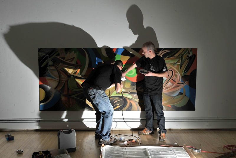 Portland graffiti artists Tim Clorius,left, and Matt W. Moore hang a piece of their aerosol art exhibit Tuesday at the University of Maine at Farmington Art Gallery.