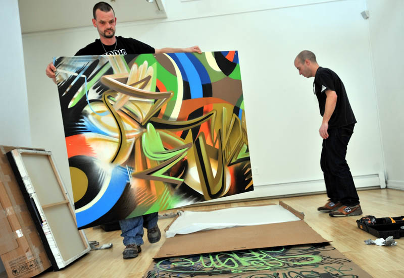 Portland graffiti artists Tim Clorius, left, and Matt W. Moore lay out pieces of their aerosol art exhibit Tuesday at the University of Maine at Farmington Art Gallery.
