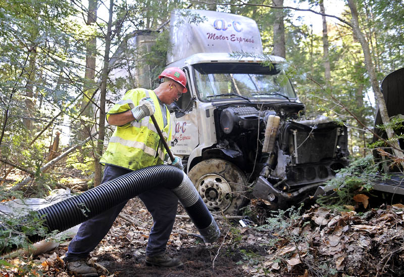 CLEAN UP ACT: CleanHarbors employee Keith Wilson vacuums fuel Wednesday from a tractor trailer that went off Interstate 95 in the northbound lane in Bowdoinham and came to rest in the woods. The driver was uninjured.