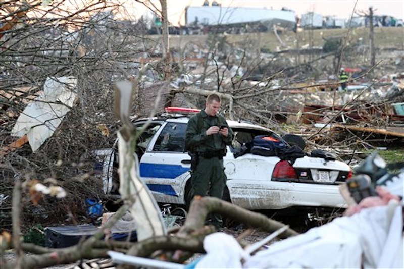 In this photo provided by SWAT Chasers via the Indianapolis Star, a police officer checks his phone while standing amid wreckage in Henryville, Ind., Friday, March 2, 2012, after a series of powerful tornadoes tore through southern Indiana, killing at least 14 people and leaving several small towns in ruin. At least one person was confirmed dead in hard-hit Henryville. (AP Photo/SWAT Chasers, Chris Bergin via the Indianapolis Star) NO SALES