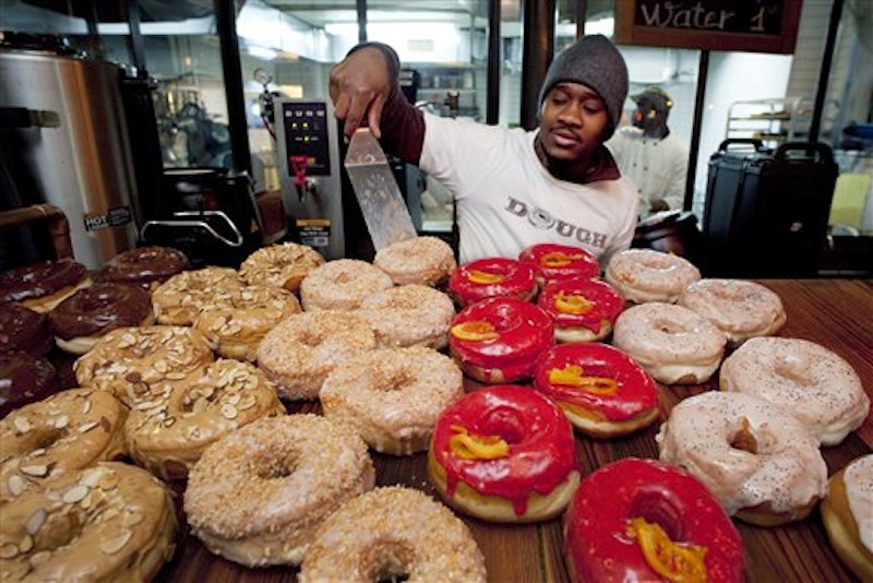 In this Feb. 24, 2012, Christian Djomatin displays freshly baked and frosted doughnuts at the Dough bakery in Brooklyn, N.Y. The small business, founded in 2010, now has 15 employees making up to 2,000 doughnuts daily, most of which are sold wholesale to outlets in Manhattan and Brooklyn. The number of people seeking unemployment benefits fell slightly last week to the lowest point in four years, a reminder that the U.S. jobs market is slowly improving. (AP Photo/Mark Lennihan) jobs;employment;small business