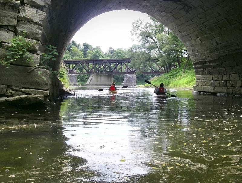 Two paddlers are seen last summer under the granite arch of bridge the carries Water Street traffic over Bond Brook in Augusta.
