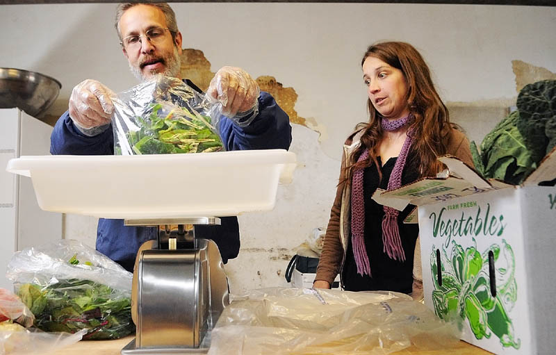 Dr. Harold Gram, left, and Sarah Miller, director of the Kennebec Local Food Initiative, weigh bags of greens as they split up large containers that came from farmers into orders for customers on market pickup day last week.