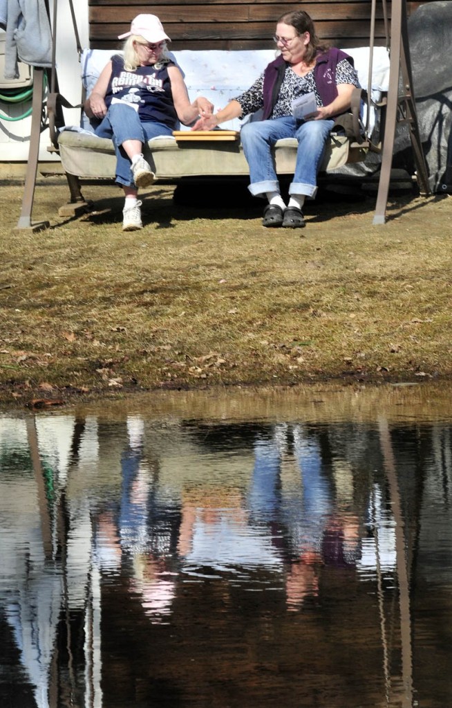 Jean Scripture, left, and Peggy Denis are reflected in a pond as they play a game of Yahtzee on a sunny and comfortable Monday. Spring officially arrived early this morning, and with more warm weather forecast for this week, the days for the seasonal pond may be numbered.
