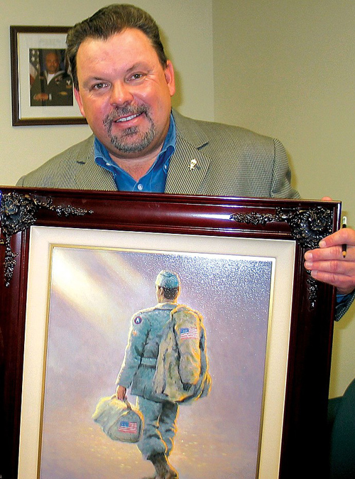 In this October 2005 photo, Thomas Kinkade holds the painting "Coming Home," depicting an American service member walking into an "ethereal" background. Kinkade created the painting based on a painting he did years earlier, also called "Coming Home," which depicted a soldier coming home for Christmas. "I took the same soldier from that painting and recreated him in a setting much more ethereal so that it wasn't a specific home because people come home to all sorts of homes. You see the soldier walking into the field of mist, and ... it could ... suggest the homecoming of soldiers who pay the ultimate price overseas or it could be the soldier who is coming home to a future — his future — which is always a mystery." (Source: Wikipedia)